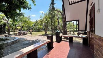 An outdoor patio area with benches and a tiled floor, surrounded by trees and greenery.