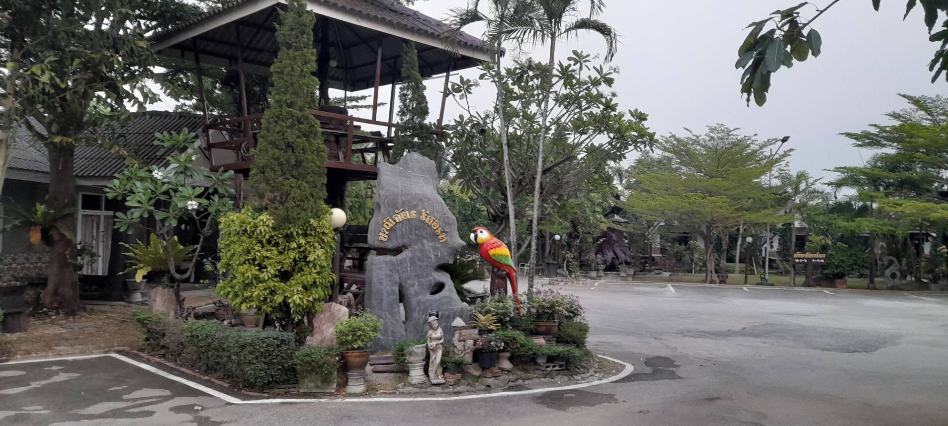A building with a unique rock-like structure, a parrot statue, and various potted plants.