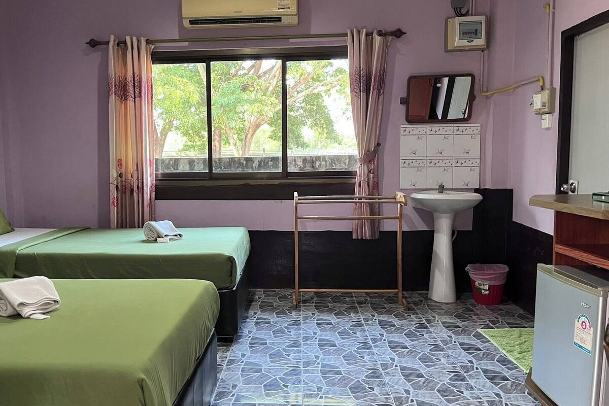 A room with two beds, a window with curtains, a sink, and a refrigerator.