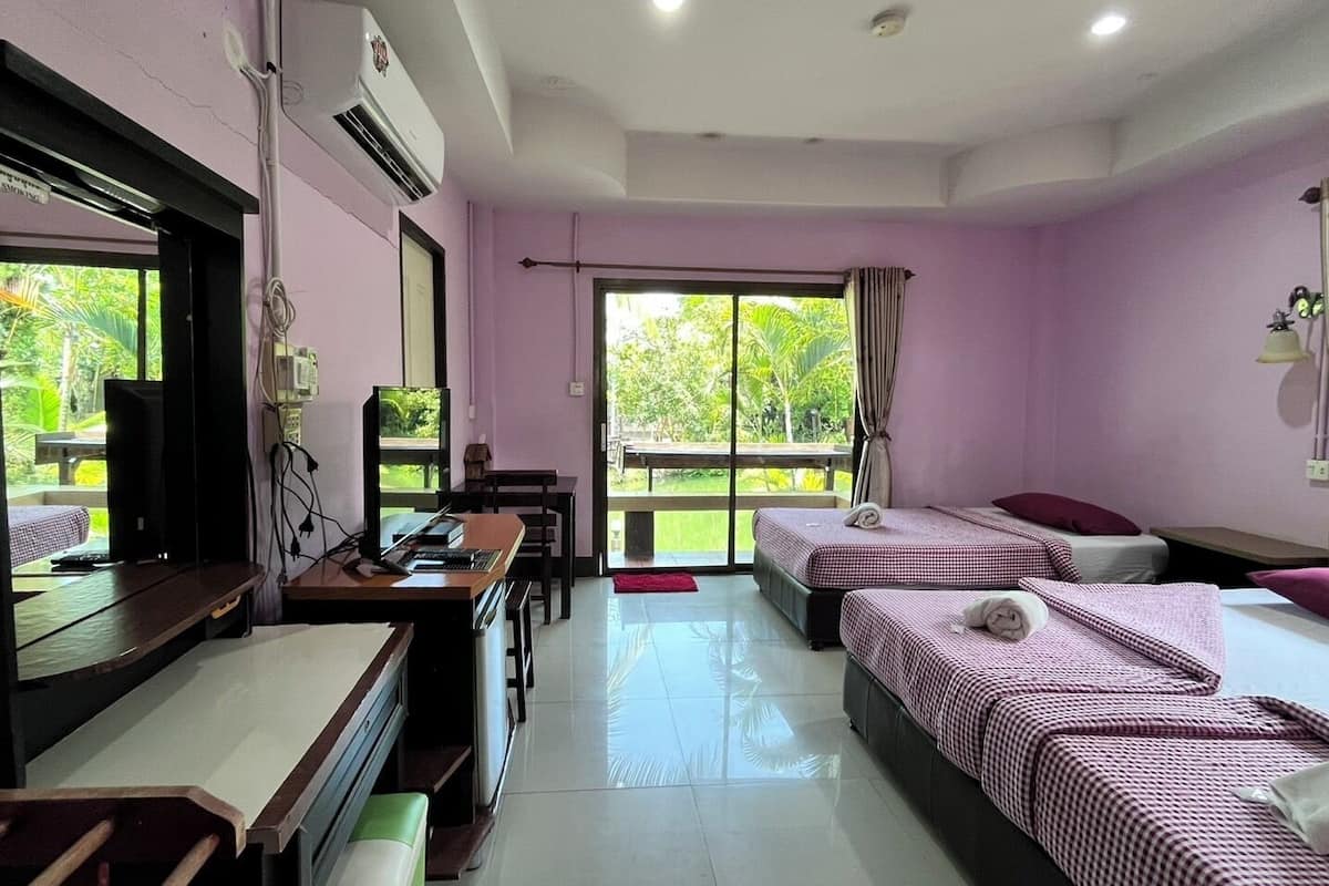A hotel room with two beds, a desk with a computer, a chair, and a large window with a view of greenery.