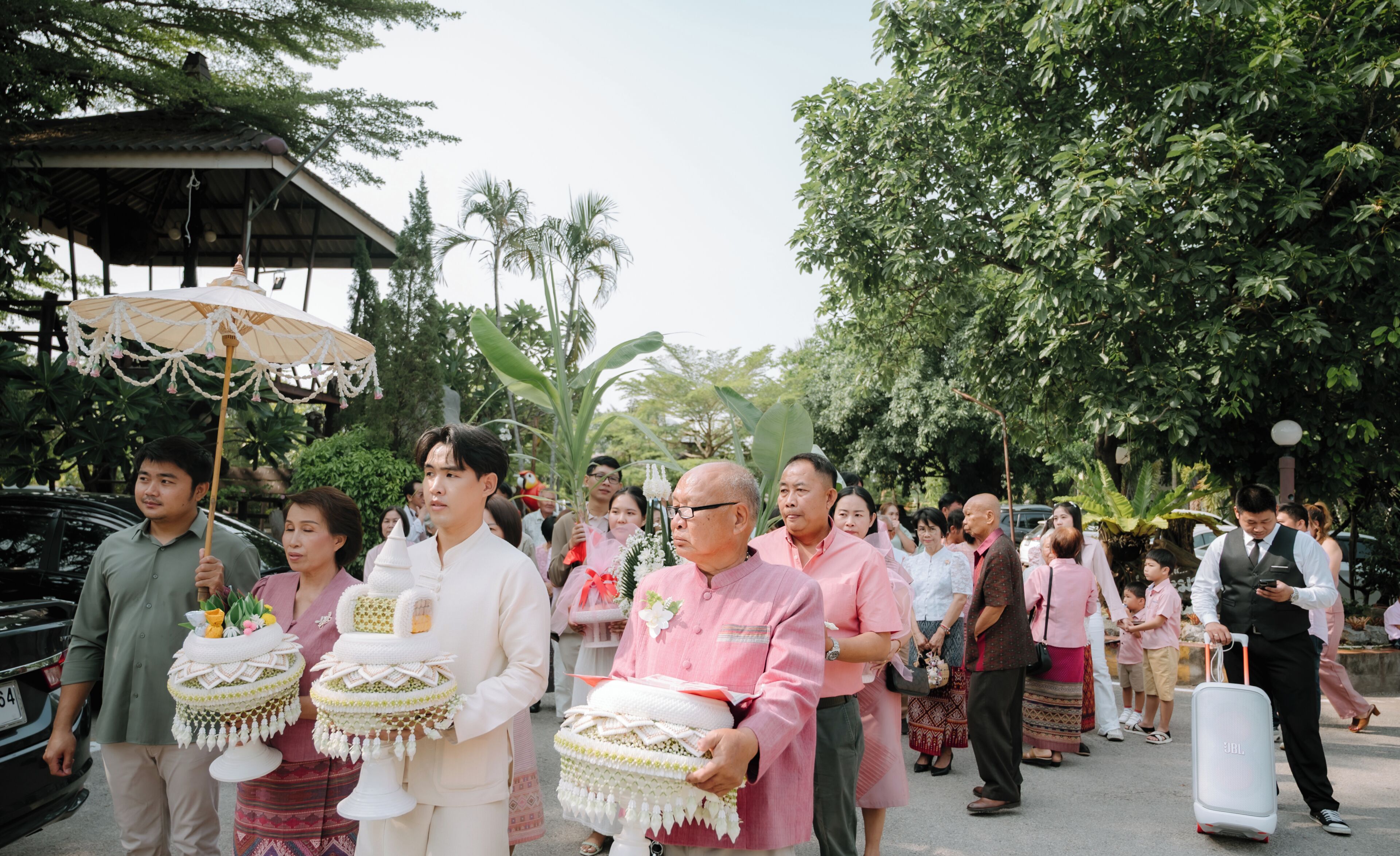A group of people in traditional attire, some holding ceremonial items, walking outdoors.