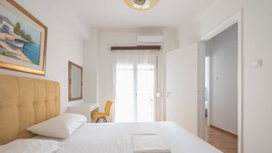 Un letto rifatto con lenzuola bianche, una sedia gialla e un quadro appeso al muro.