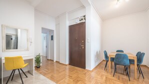 Un'elegante sala da pranzo con pavimento in parquet a spina di pesce, una scrivania bianca con sedia gialla e un tavolo da pranzo con sedie blu.