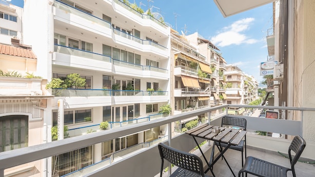 Un balcone con tavolo e sedie, affacciato su una zona residenziale con diversi edifici.