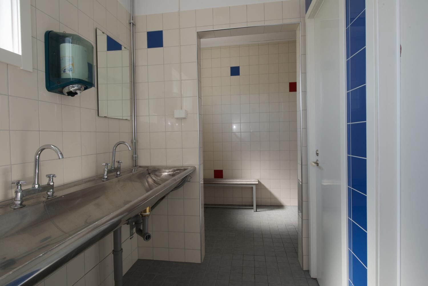 A modern bathroom with a long sink, a mirror, and a bench in the shower area.