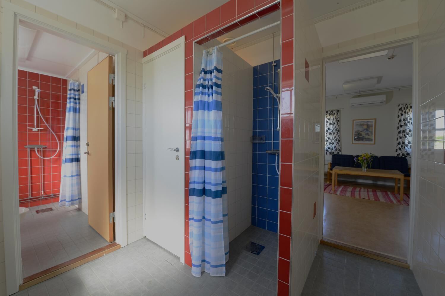 A bathroom with a shower, a toilet, and a sink. There is a door leading to a living area with a sofa and a table.
