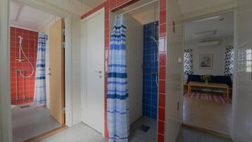 A bathroom with a shower, a toilet, and a sink. There is a door leading to a living area with a sofa and a table.