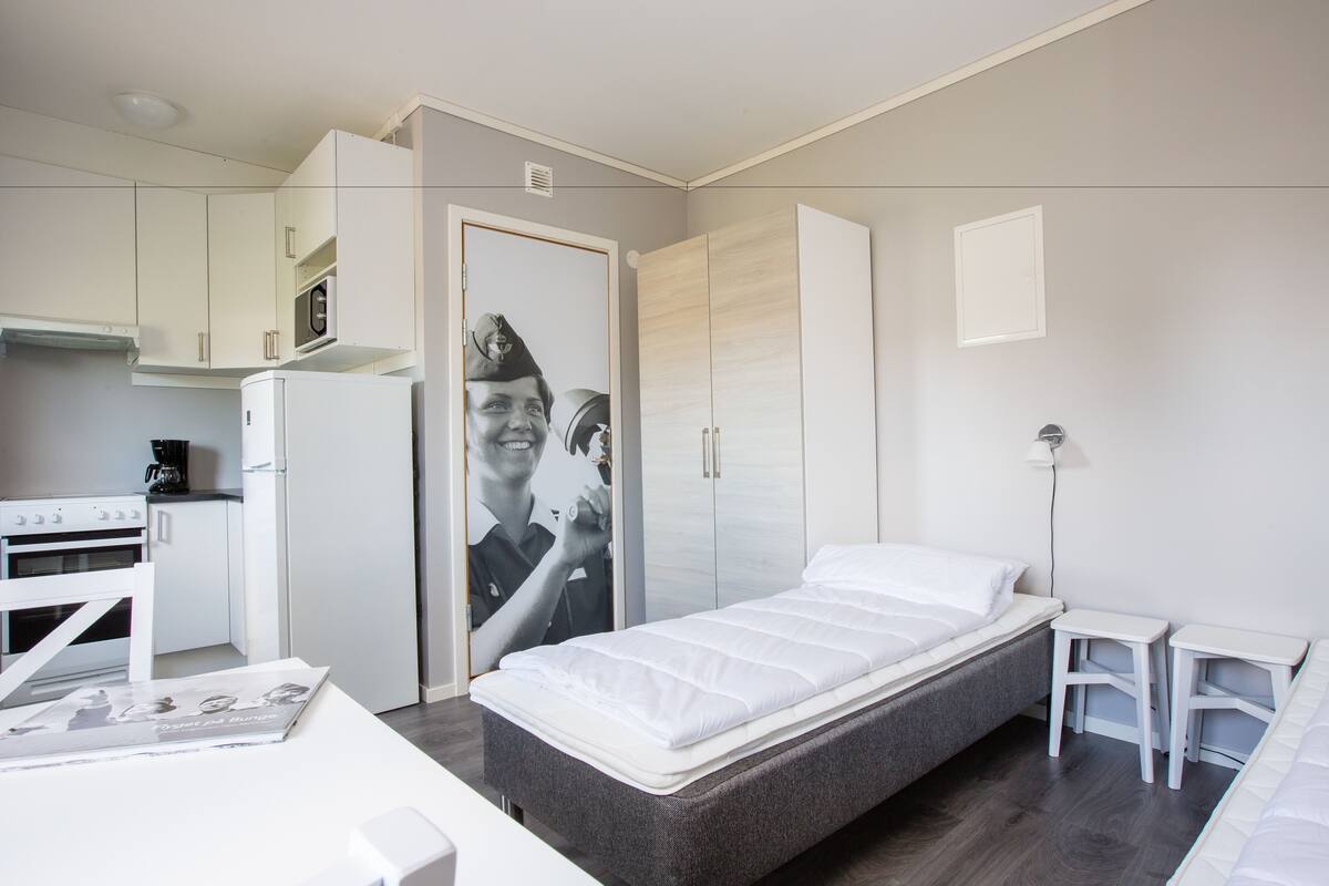Ein gemütliches Schlafzimmer mit Bett, kleinem Schreibtisch, Kleiderschrank und Küchenzeile.