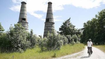 A person riding a bicycle on a dirt path with two large industrial chimneys in the background.