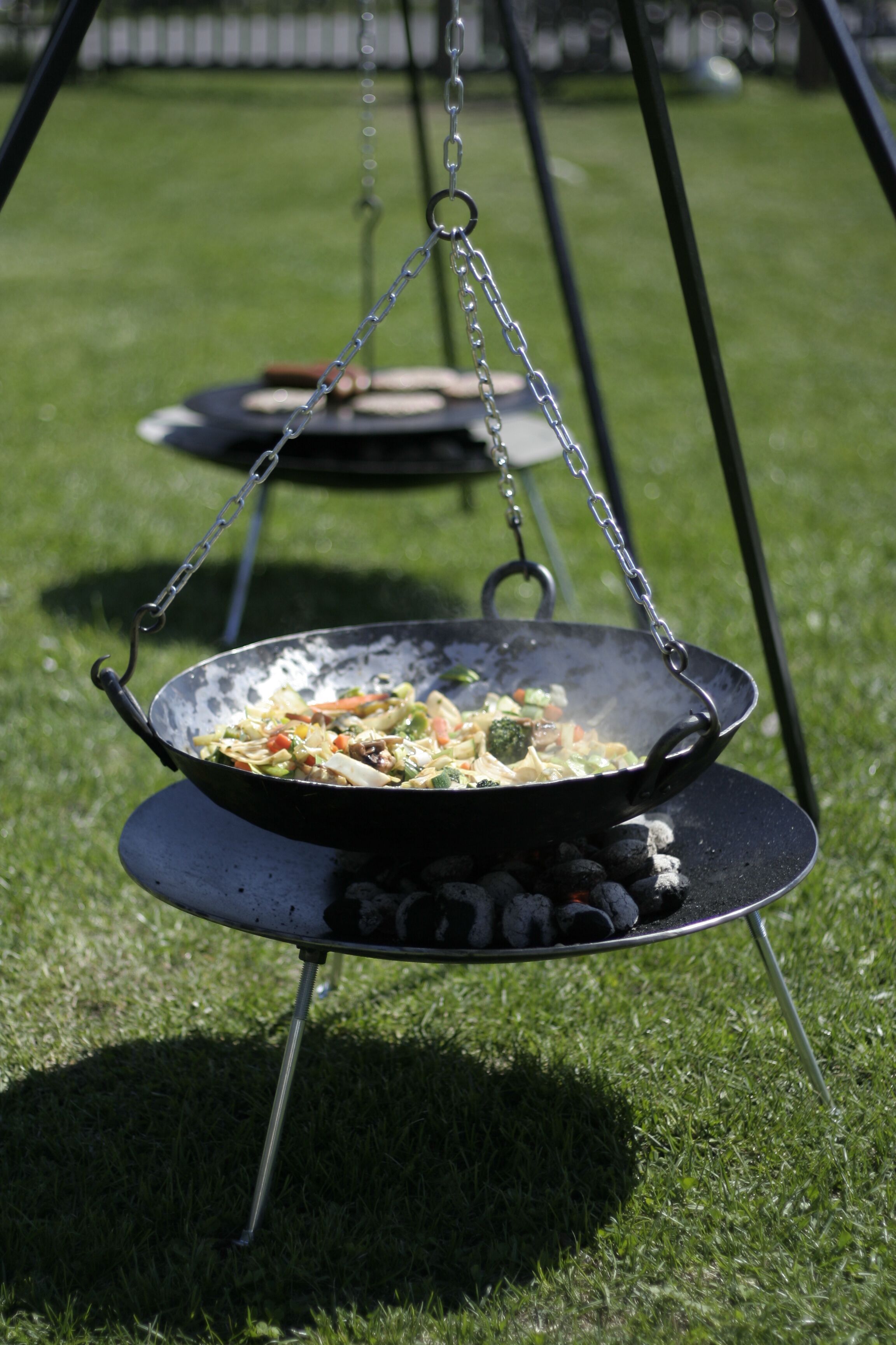 A wok on a portable grill with vegetables, set on a grassy lawn.