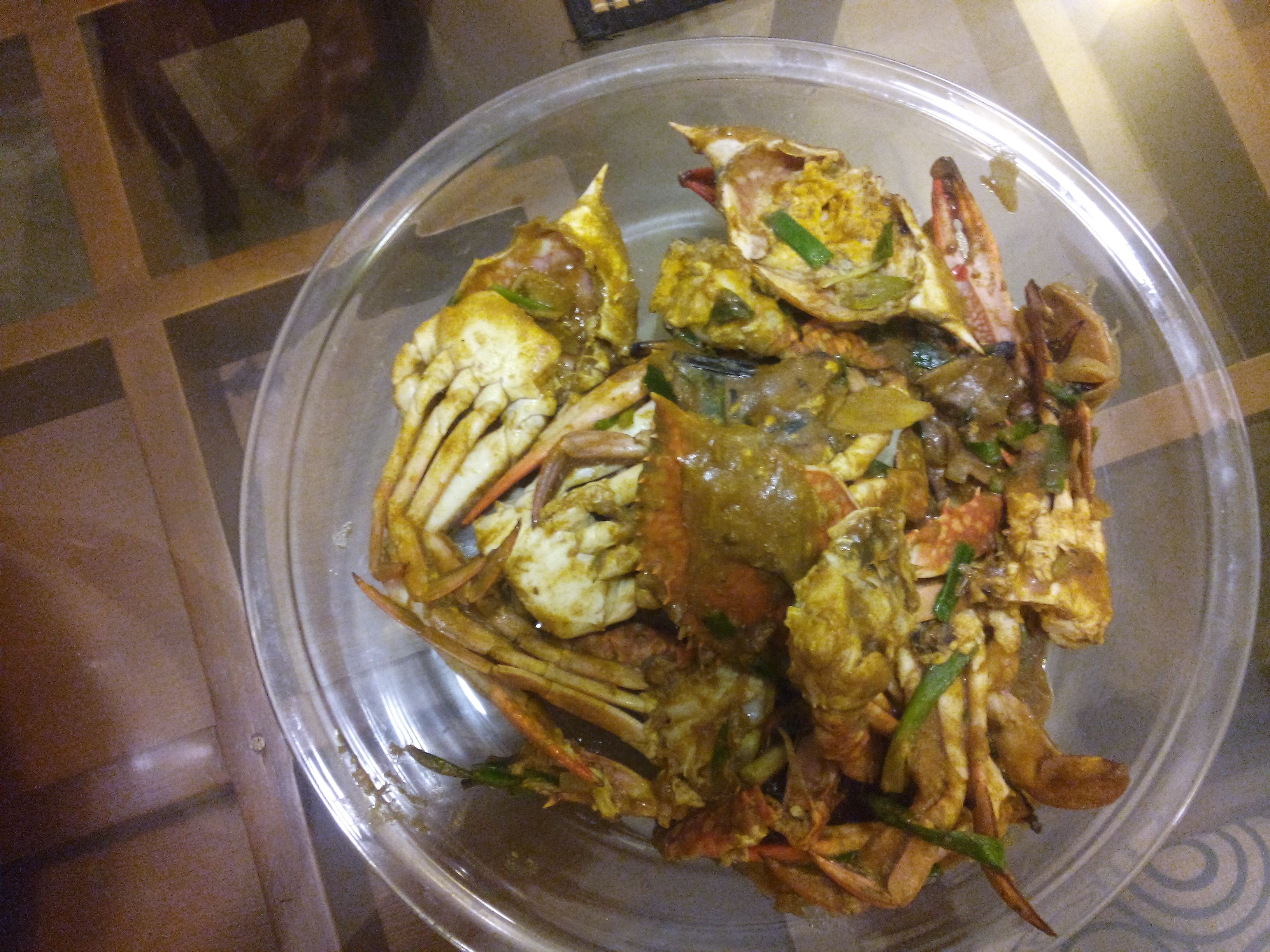 A clear plastic bowl containing a seafood dish with crab, green vegetables, and a yellow sauce.