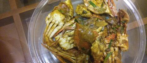 A clear plastic bowl containing a seafood dish with crab, green vegetables, and a yellow sauce.