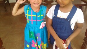 Two children standing indoors, one in a colorful dress and the other in overalls. - Bandhusena Apartments (Mirissa)
