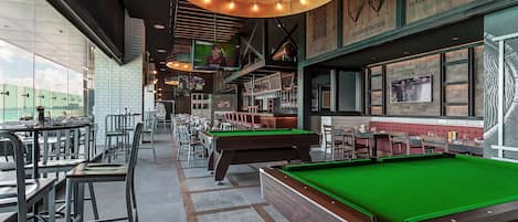 Una sala de billar con mesas y sillas, una mesa de pool y una zona de bar con asientos.