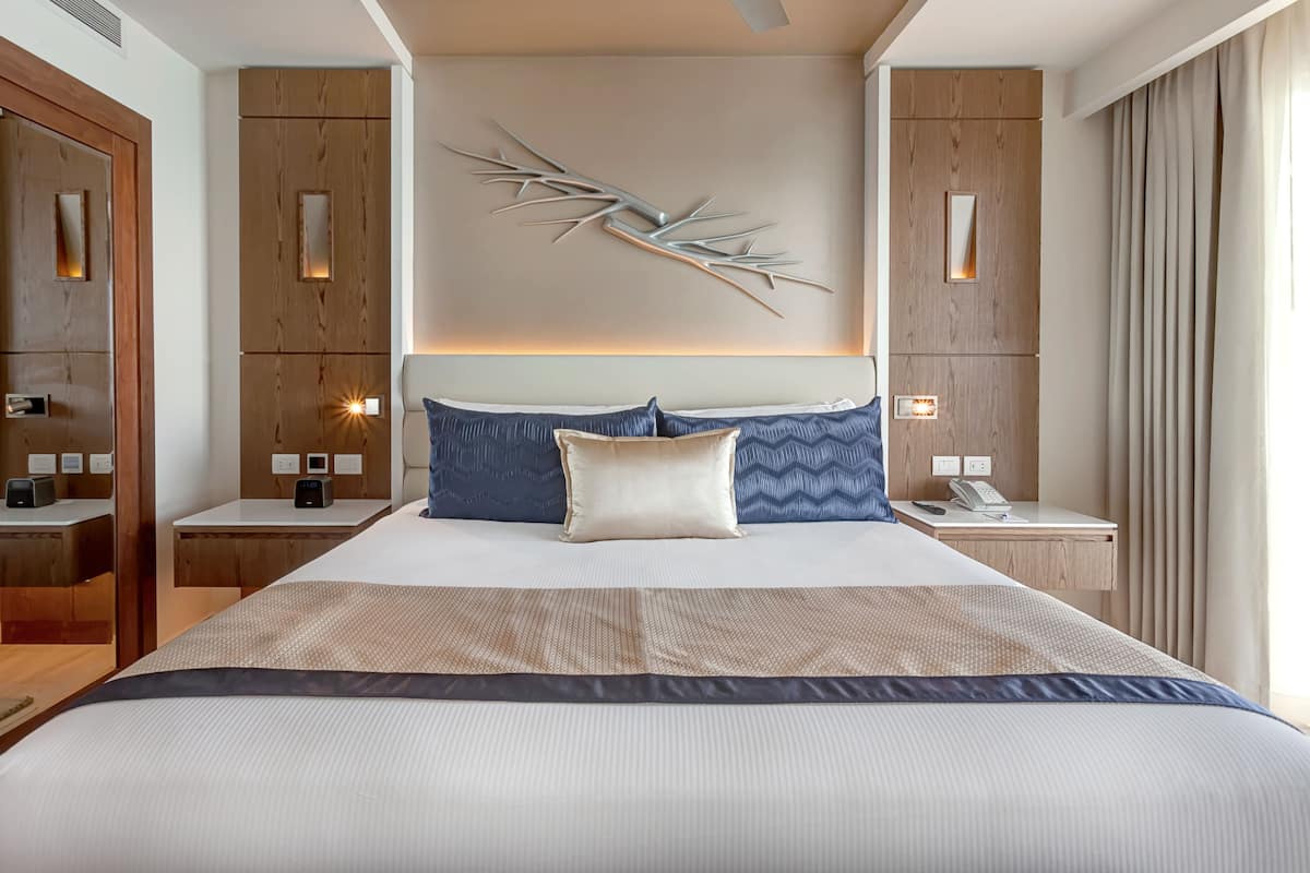 A modern hotel room with a large bed, wooden paneling, a decorative wall piece, and bedside lamps.
