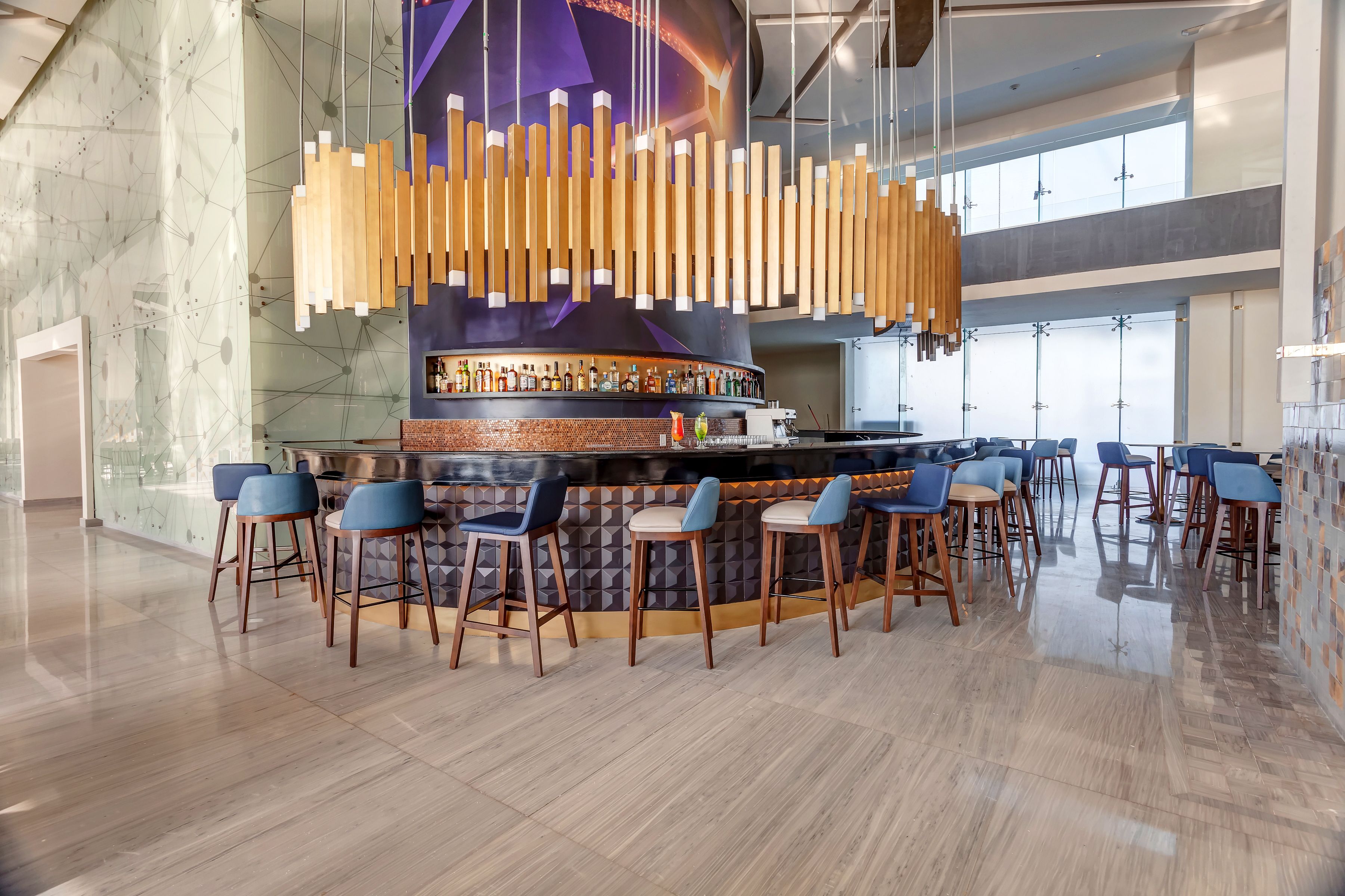 Een moderne bar met een centraal gelegen toog, verschillende krukken en een hangende lamp.