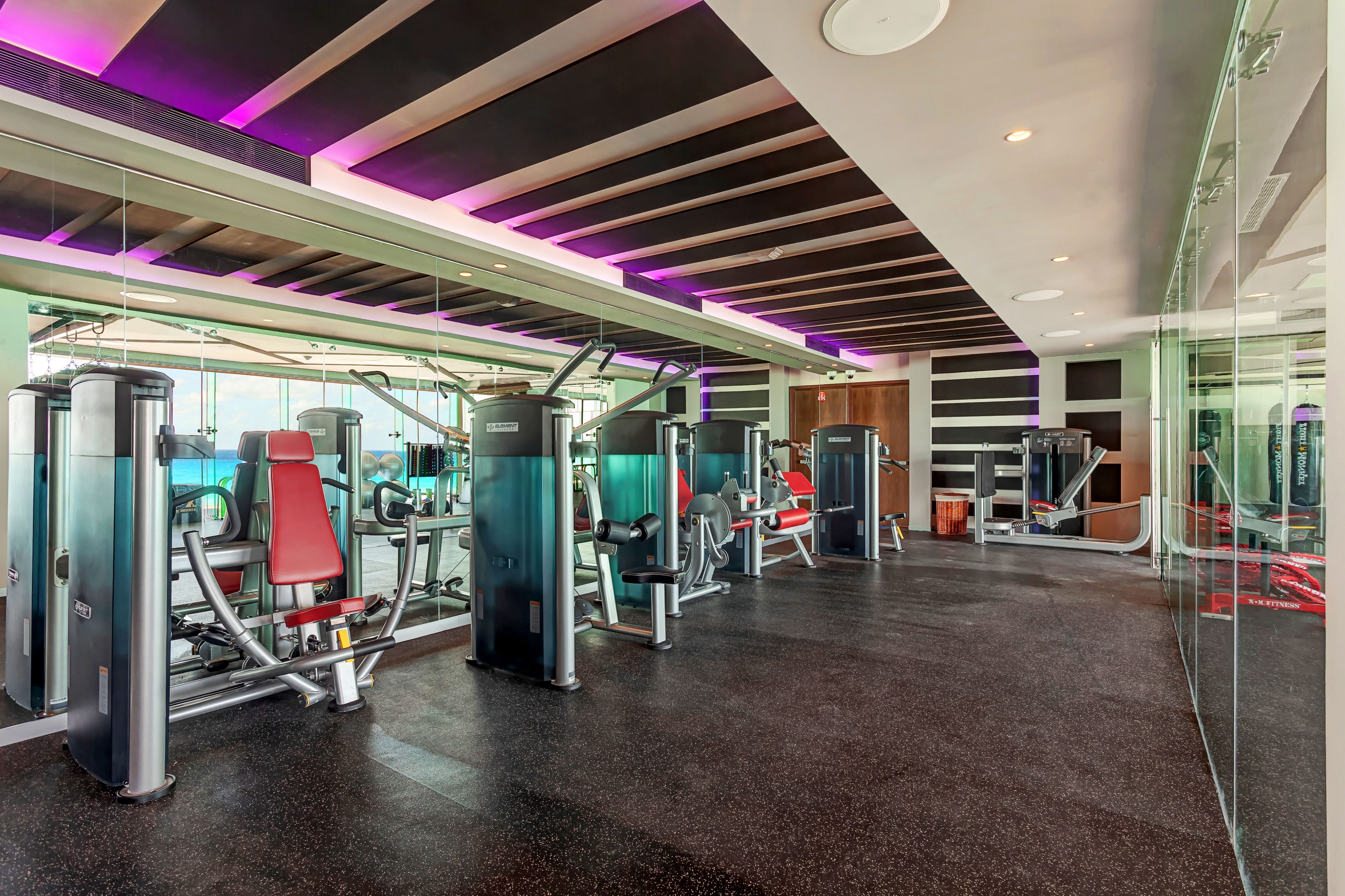 Une salle de sport moderne dotée de divers appareils d’exercice, de murs en verre et d’un design contemporain au niveau du plafond.