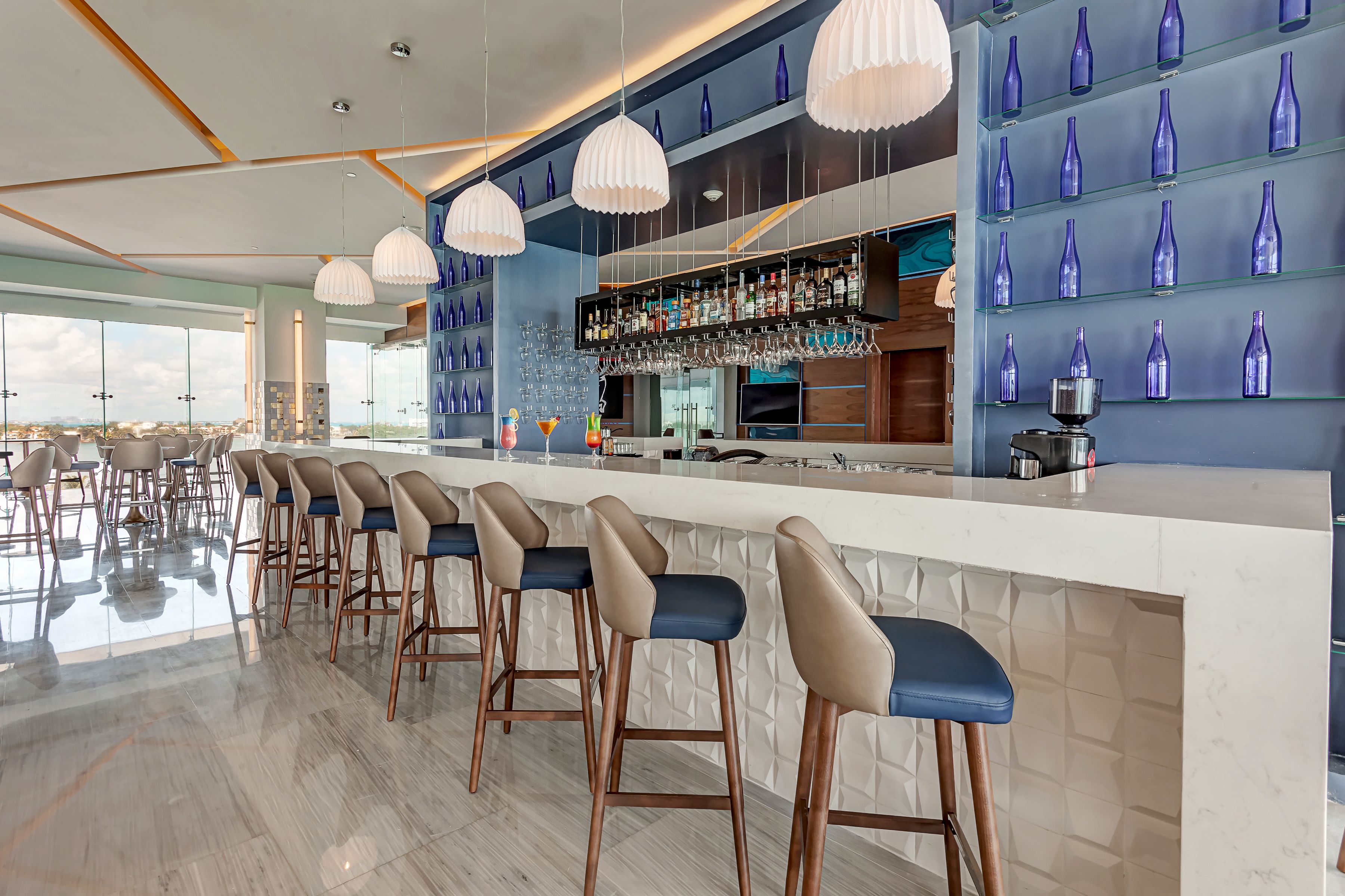 A modern bar area with high stools, a bar counter, and shelves of blue bottles.
