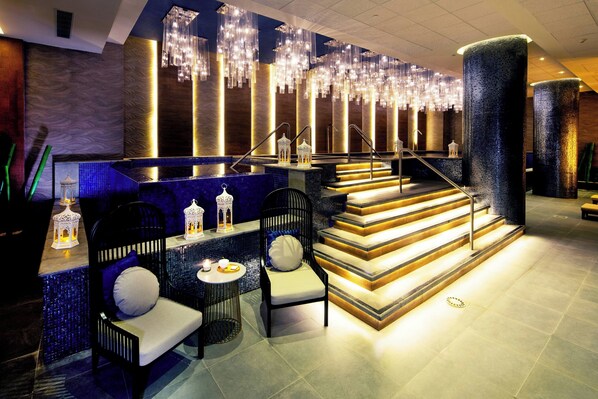 A modern lobby with a blue mosaic wall, a staircase, and seating areas.