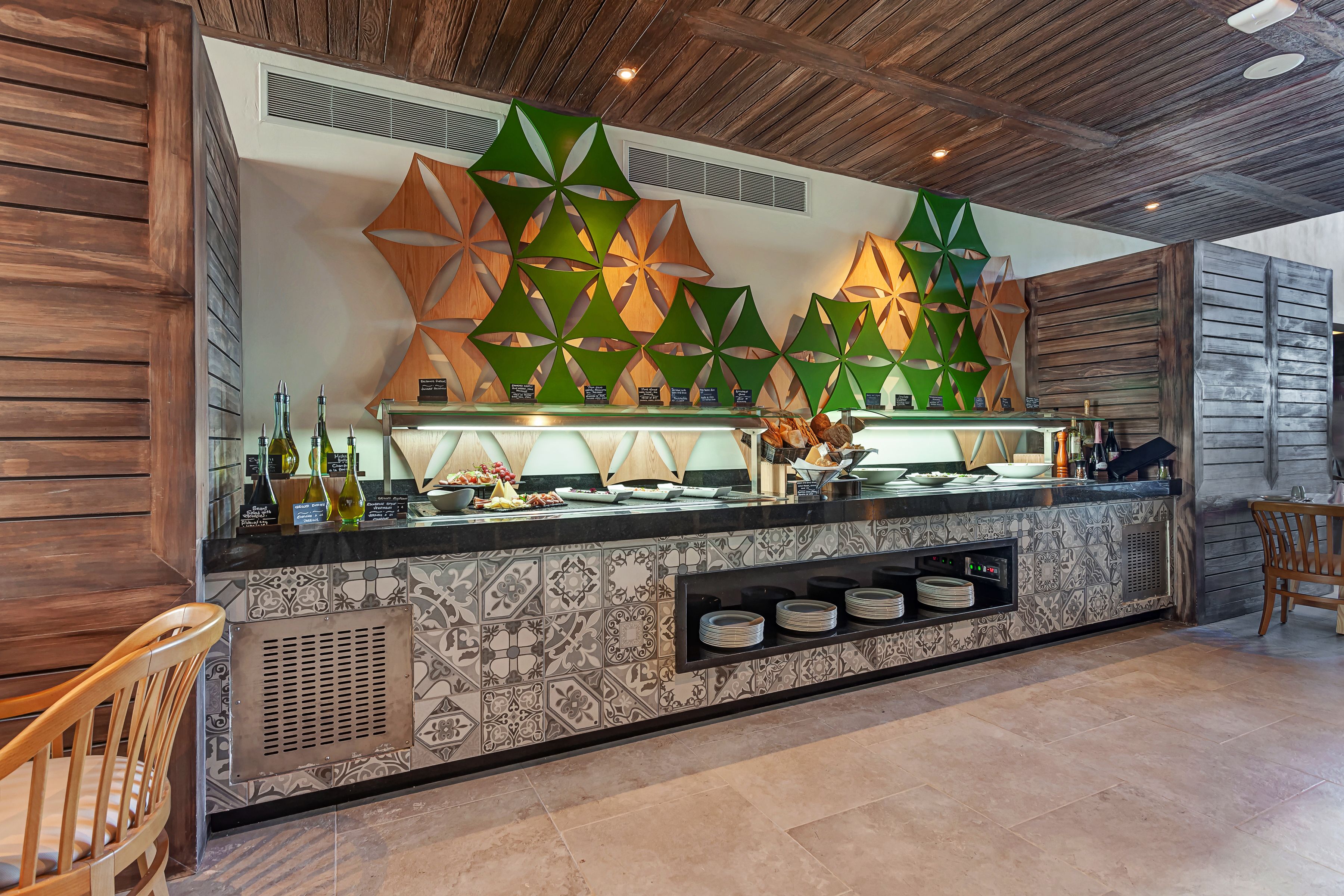 Un espace bar moderne avec un mur au motif géométrique, un pare-feu en carreaux et une variété d’ustensiles et de bouteilles de bar.