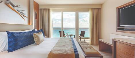 A hotel room with a large bed, a desk, a television, and a balcony with a view of the sea.