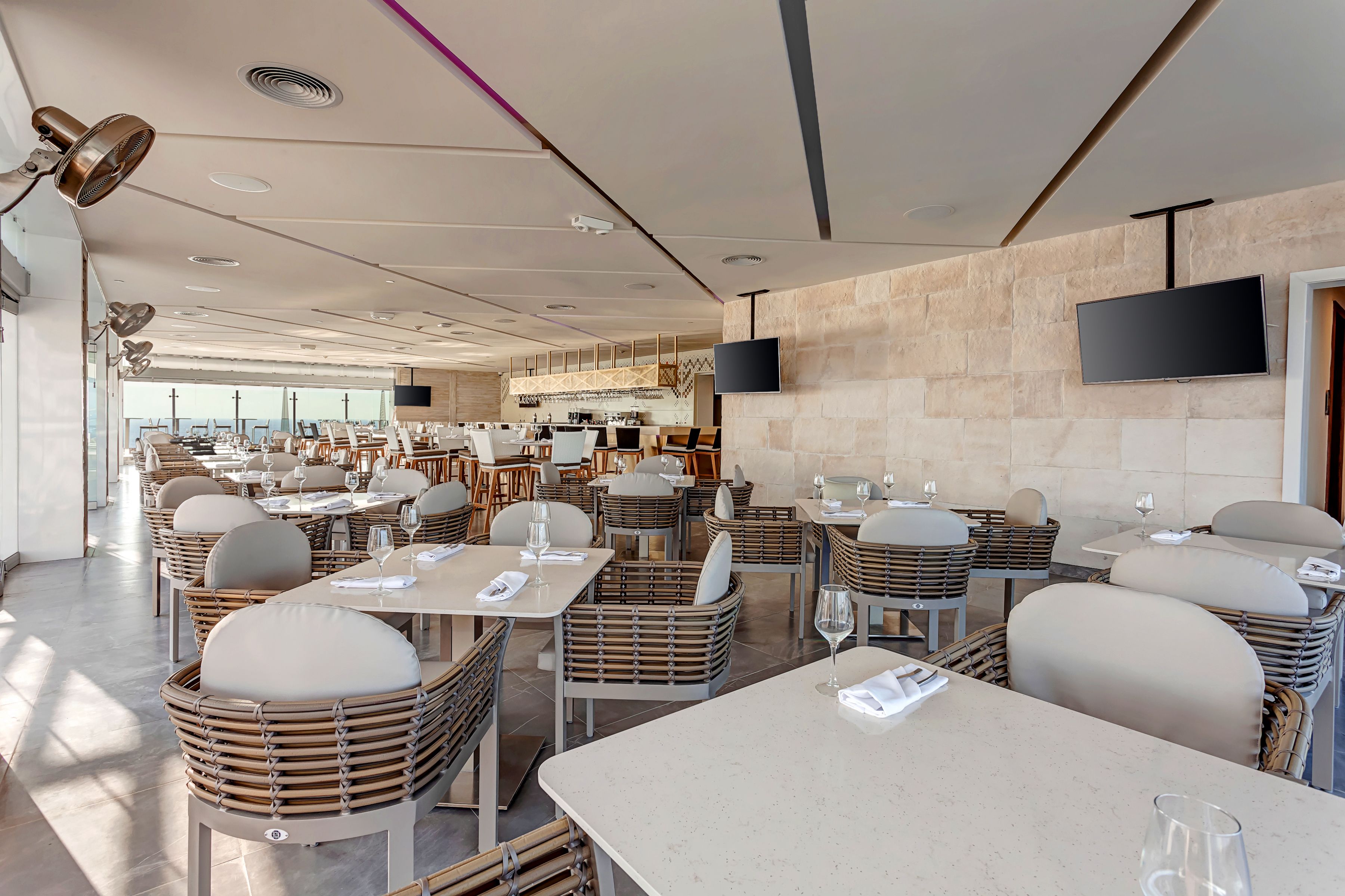 A modern restaurant with wicker furniture, flat-screen TVs, and a view of the city.