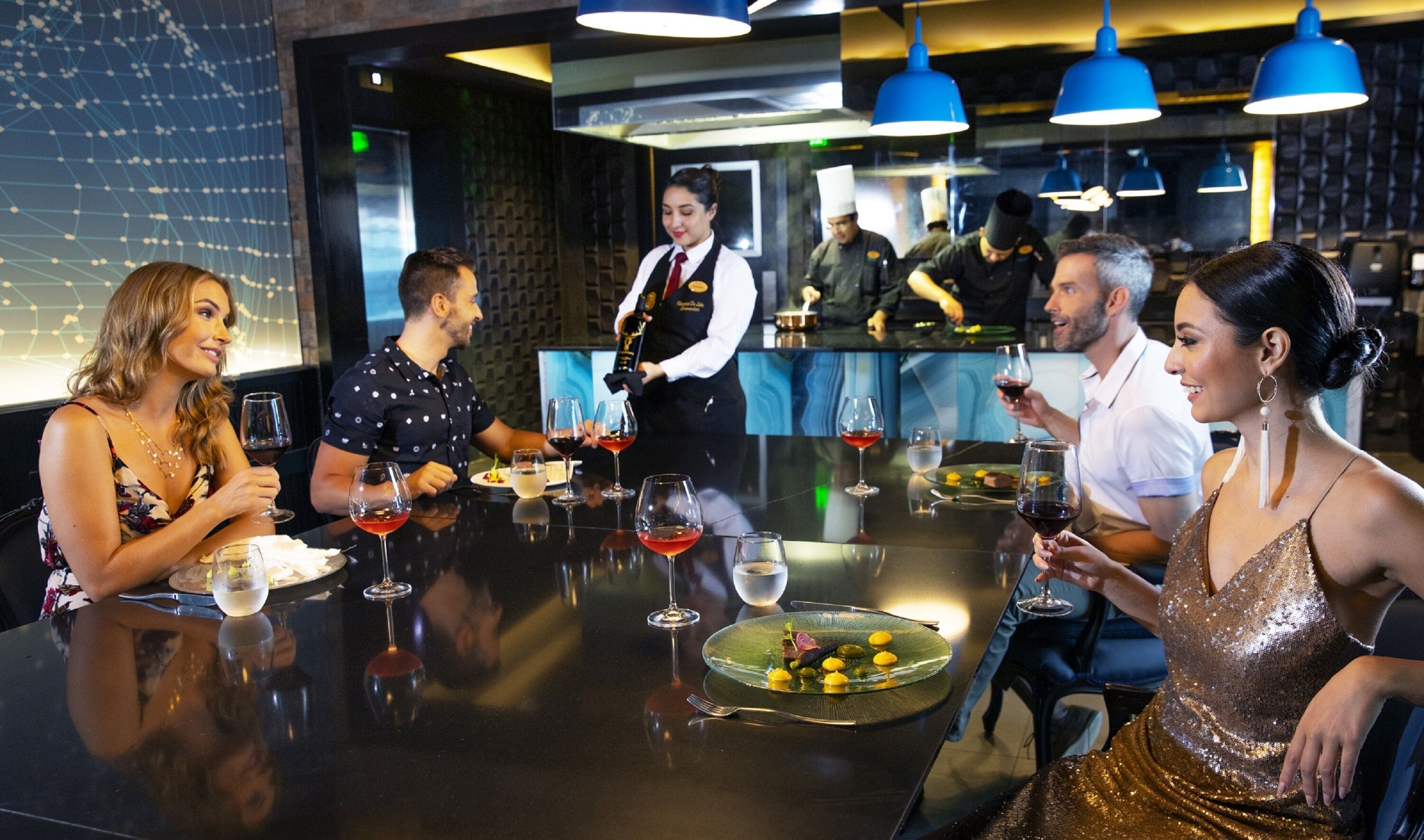 A restaurant interior with a modern design, featuring a black table with wine glasses and plates, and a waiter in uniform.