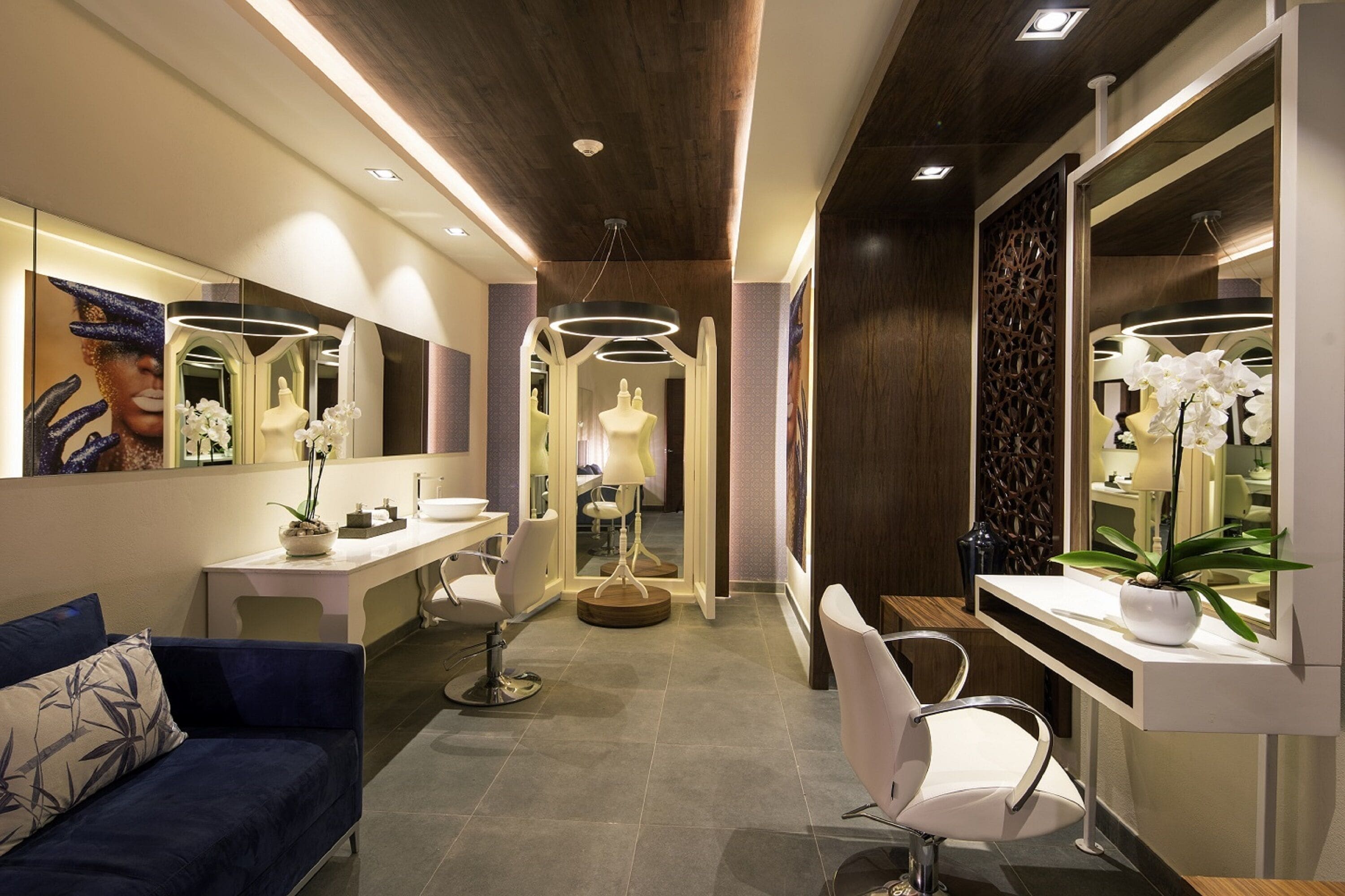 A modern salon with a reception desk, two white chairs, a blue sofa, and a large mirror.