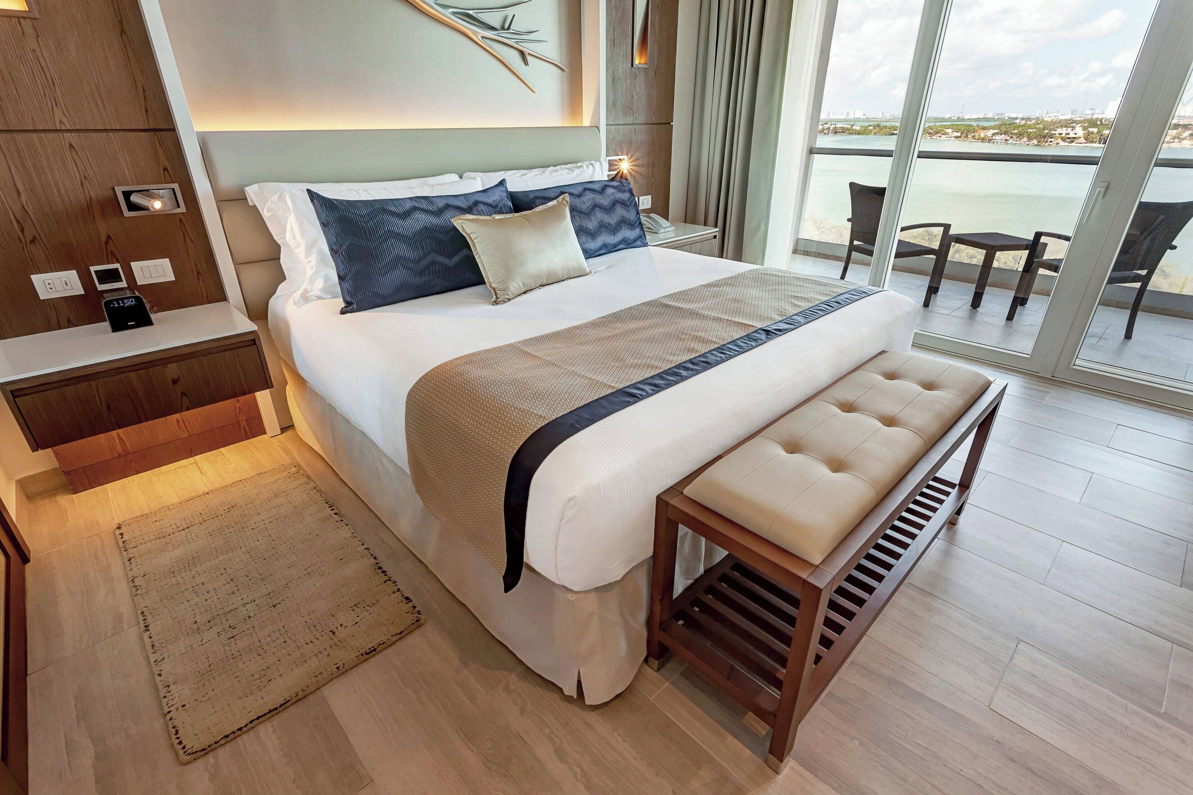 Une chambre d’hôtel moderne dotée d’un grand lit, d’une table de chevet avec un téléphone, d’une lampe de chevet et offrant une vue sur la mer grâce à de grandes fenêtres.