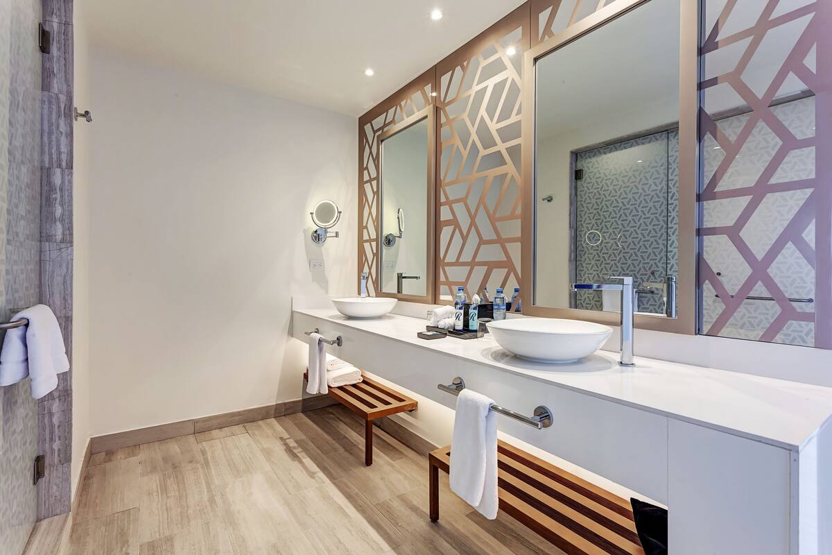 A modern bathroom with two sinks, a large mirror, and a wooden bench.