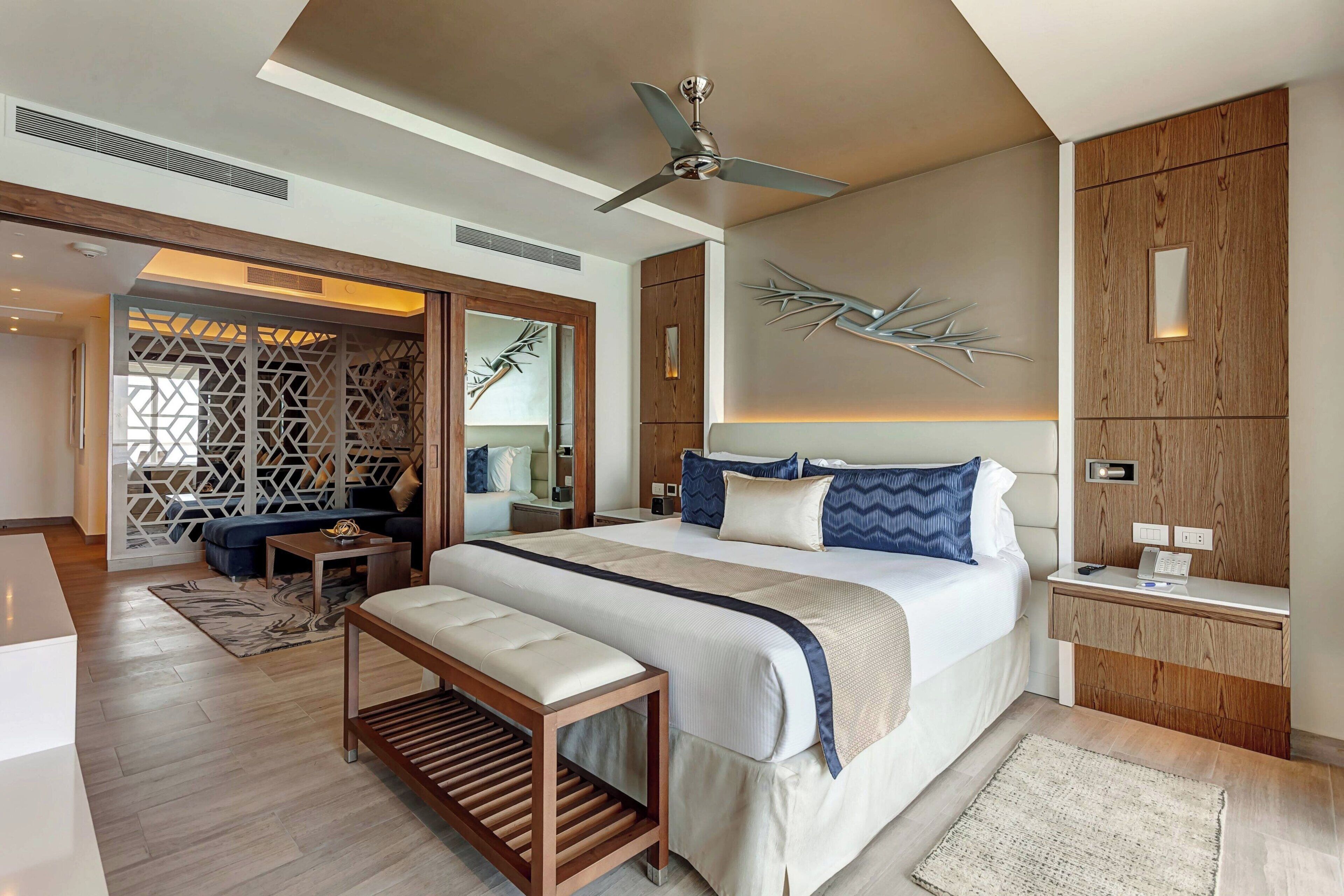 A modern hotel room with a large bed, a desk, a bench, and a ceiling fan.