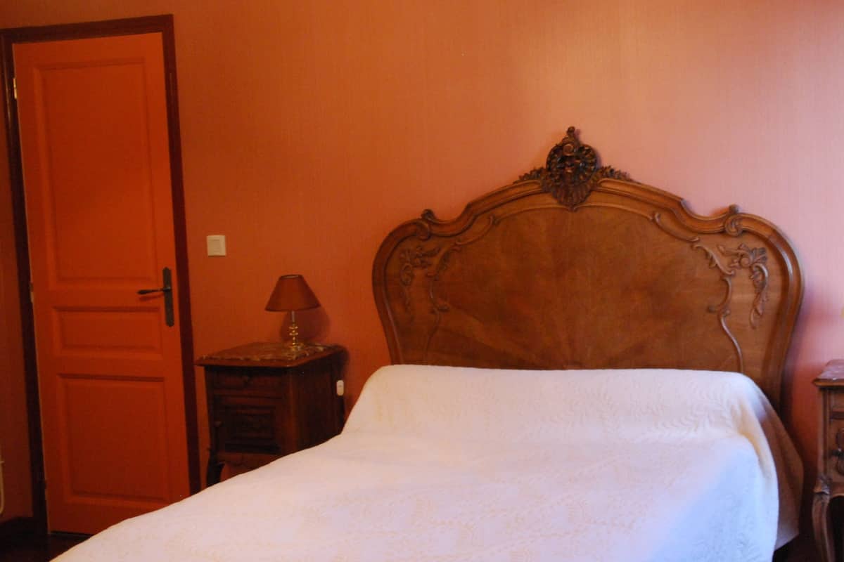 A neatly made bed in a room with a wooden headboard, a wooden nightstand with a lamp, and a closed door.