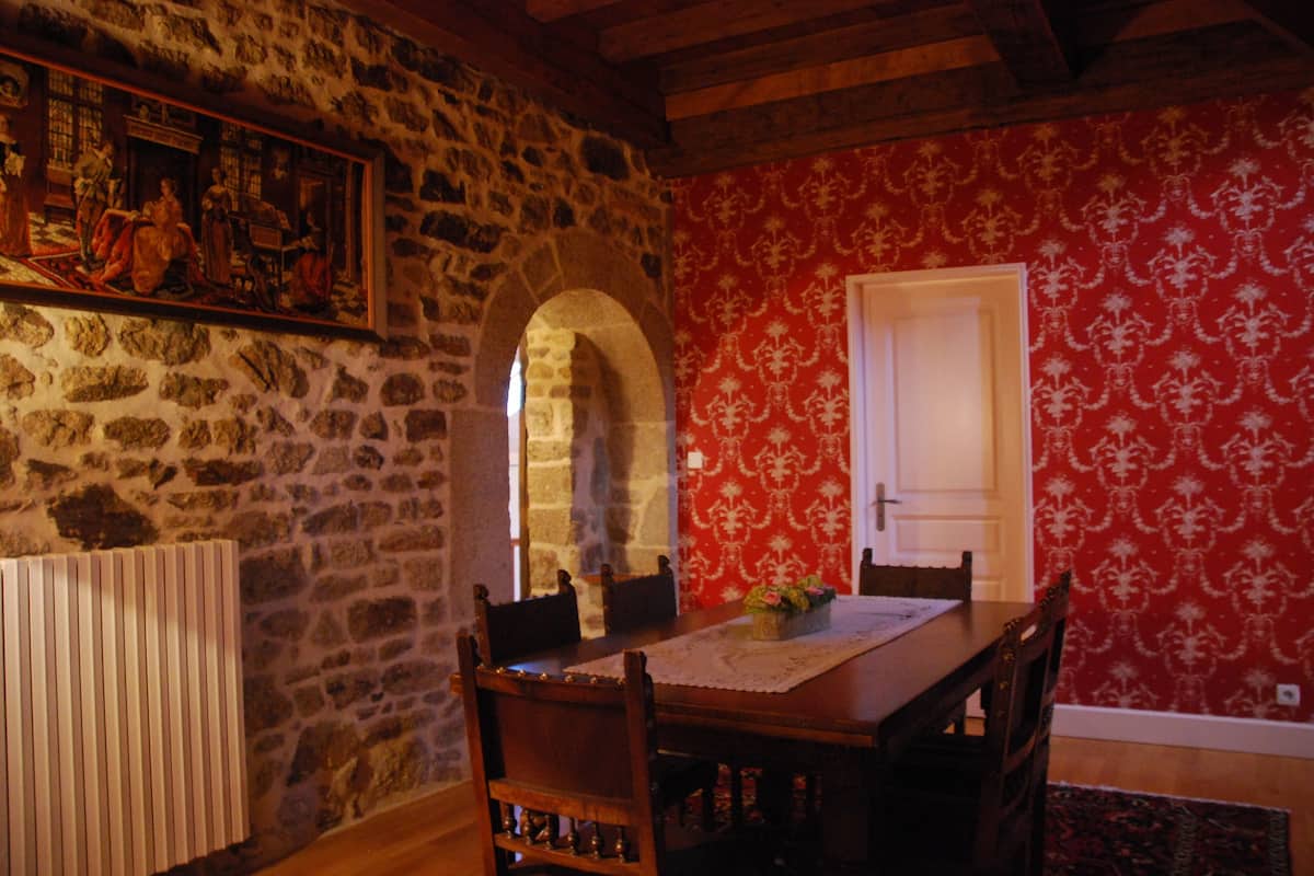 A dining area with a stone wall, a red patterned wall, and a wooden table with chairs.