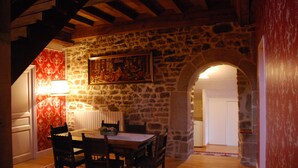 A dining area with a stone wall, wooden ceiling beams, a table with chairs, a red patterned wall, and a painting above the table. - Au Domaine de Rimou (Rimou)