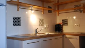A kitchen with white cabinets, a stainless steel sink, and wooden shelves. - Au Domaine de Rimou (Rimou)