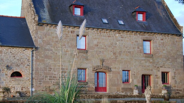 A stone building with a sloped roof, multiple windows with red frames, and a central entrance. - Au Domaine de Rimou (Rimou)
