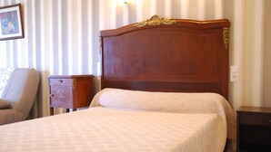 A neatly made bed with a patterned bedspread, a wooden headboard, a bedside table, and a chair. - Au Domaine de Rimou (Rimou)