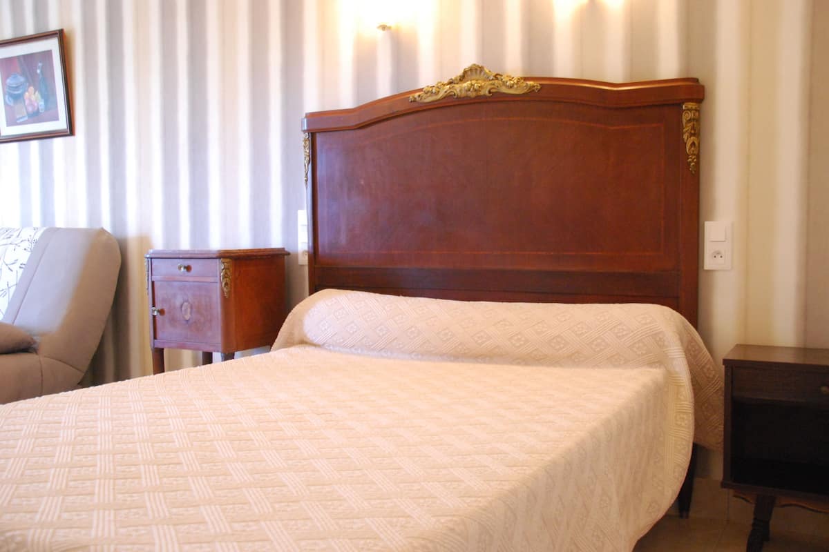 A neatly made bed with a patterned bedspread, a wooden headboard, a bedside table, and a chair.