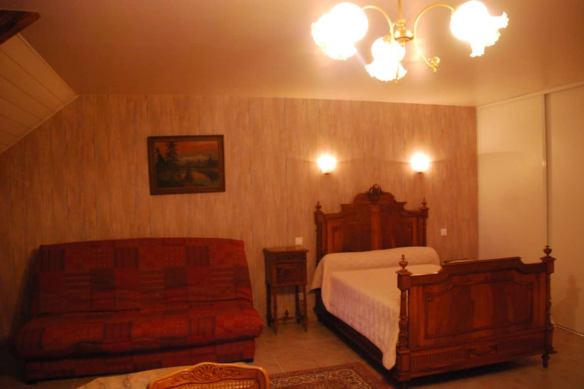 A bedroom with a wooden bed, a red sofa, and a small bedside table.