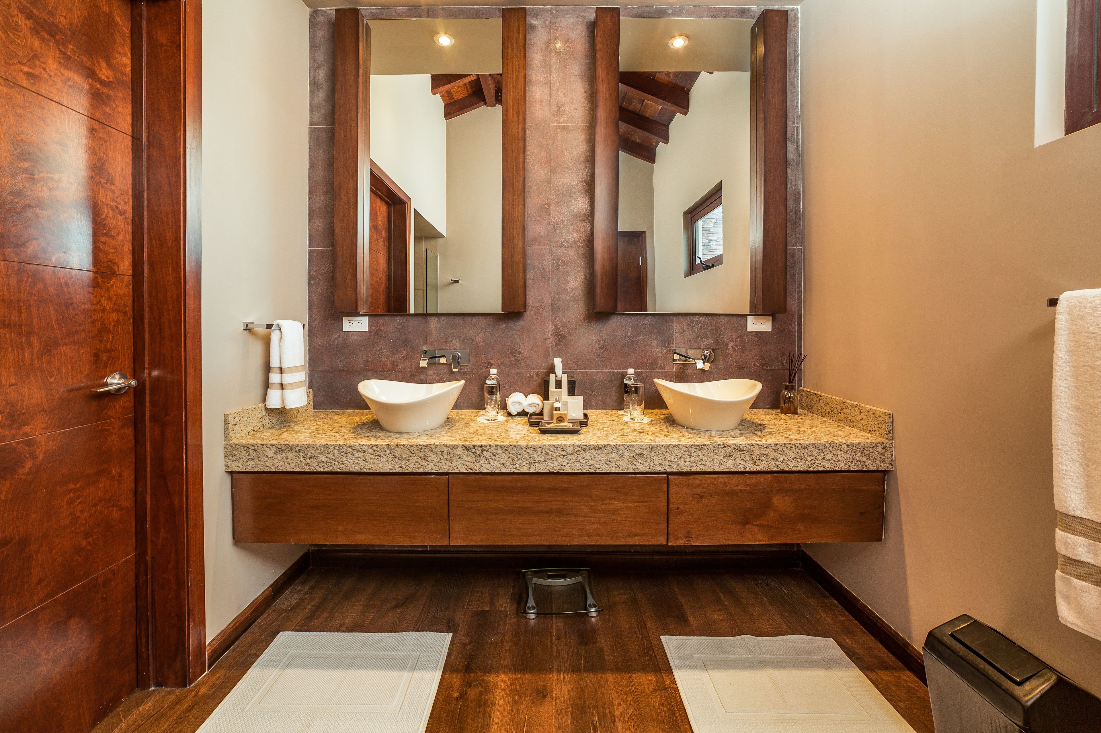 A bathroom with two sinks, wooden vanity, large mirror, and a wooden door.