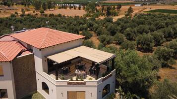 Edificio de dos plantas con tejado de tejas rojas, zona de estar al aire libre y vistas a olivares y montañas.
