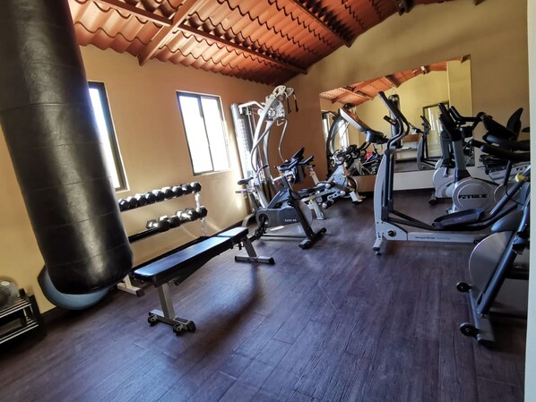 Un gimnasio con diversos equipos de ejercicio, una banca y un saco de boxeo.