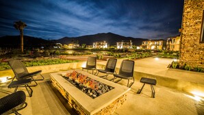 An outdoor patio area with a fire feature, lounge chairs, and a view of a mountain at night.