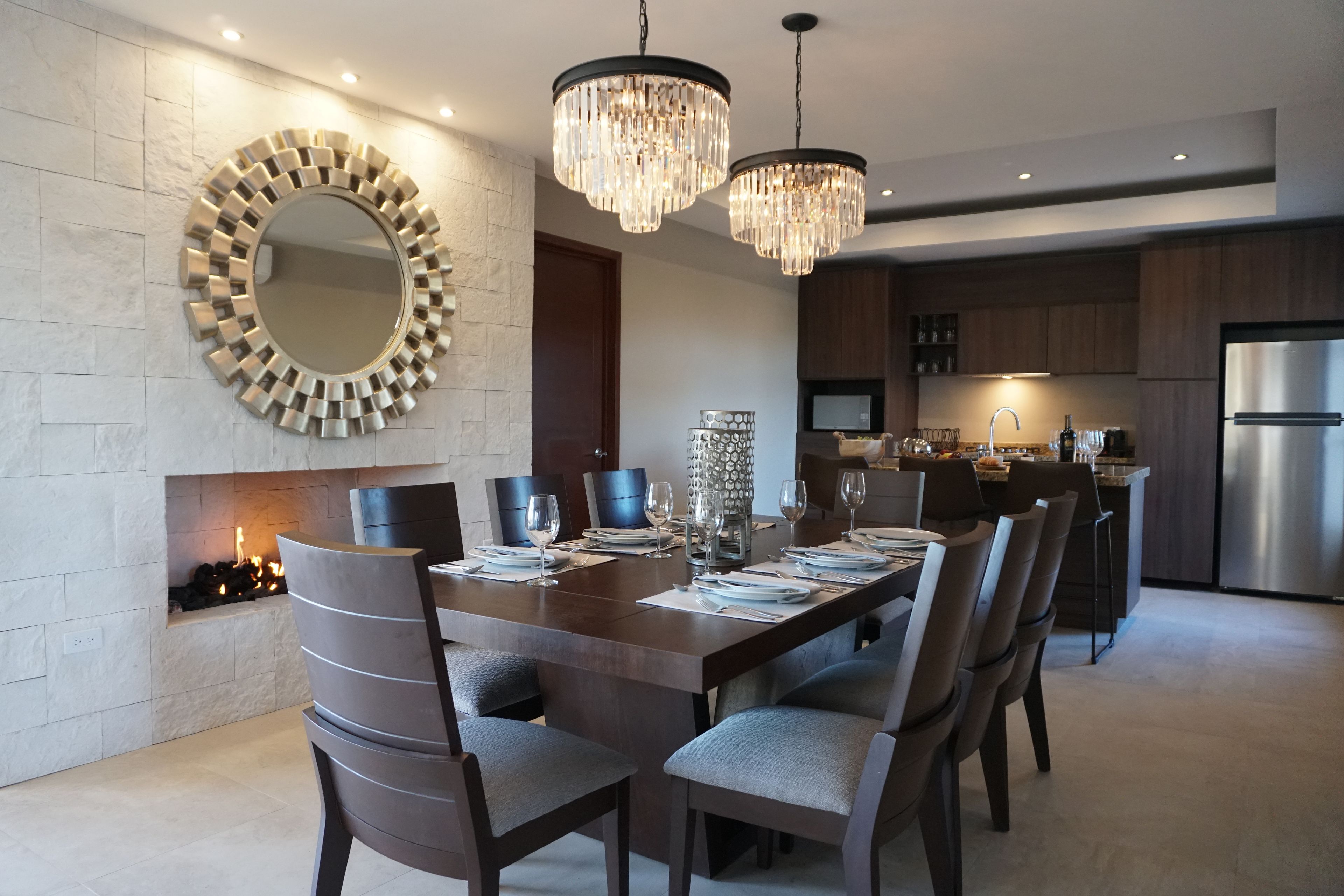Un comedor moderno con un espejo redondo grande, chimenea y una araña.