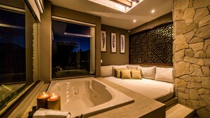 A modern spa room with a large bathtub, a sofa with cushions, and a stone wall.
