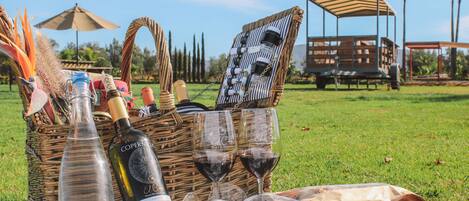 Un montaje para picnic con una cesta de mimbre, botellas de vino, copas y una mesa sobre un campo cubierto de césped.