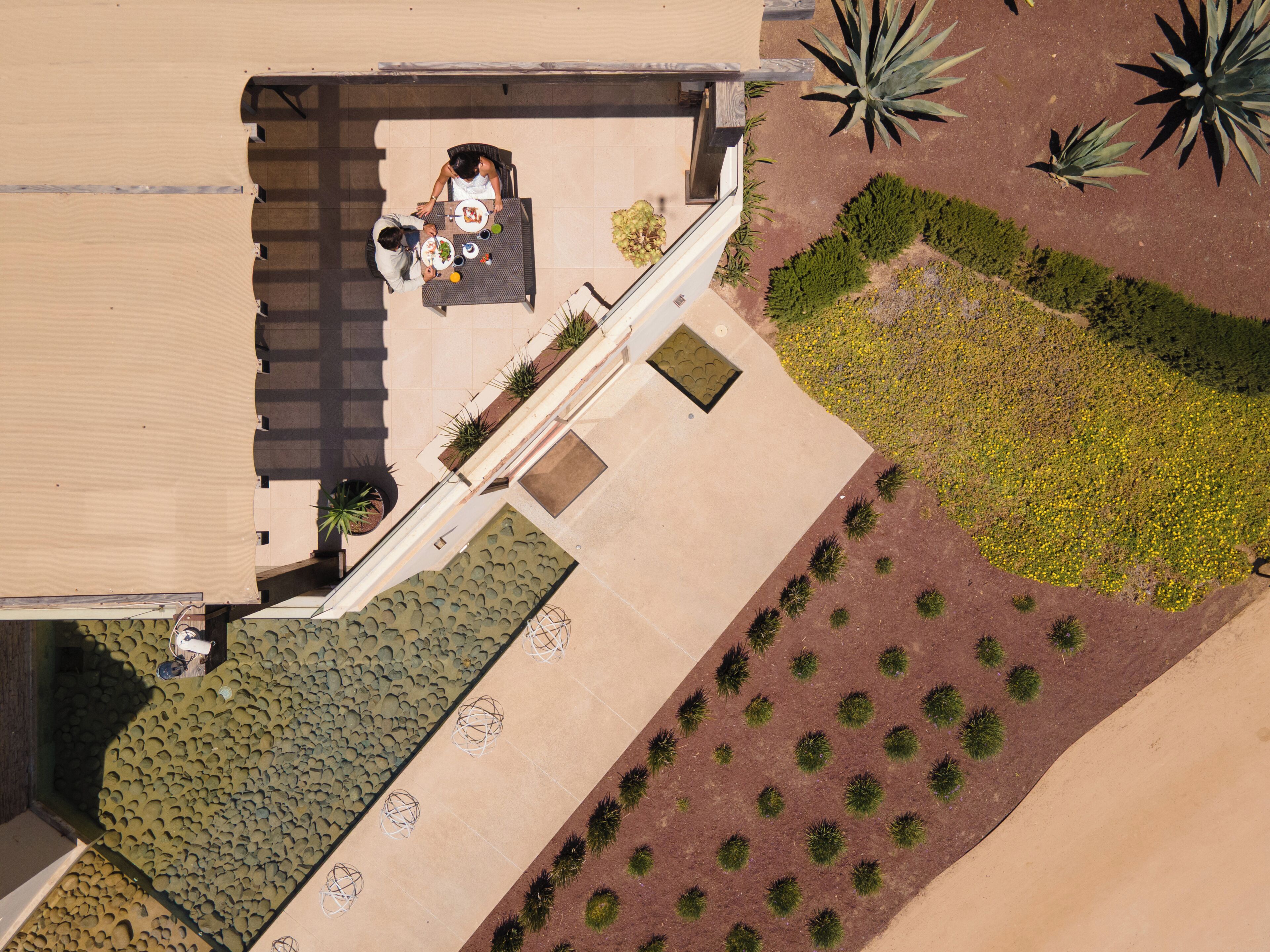 An aerial view of a rooftop terrace with a dining table, chairs, and potted plants.