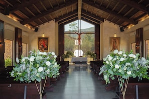 An interior with wooden beams, pews, altar, and floral arrangements.