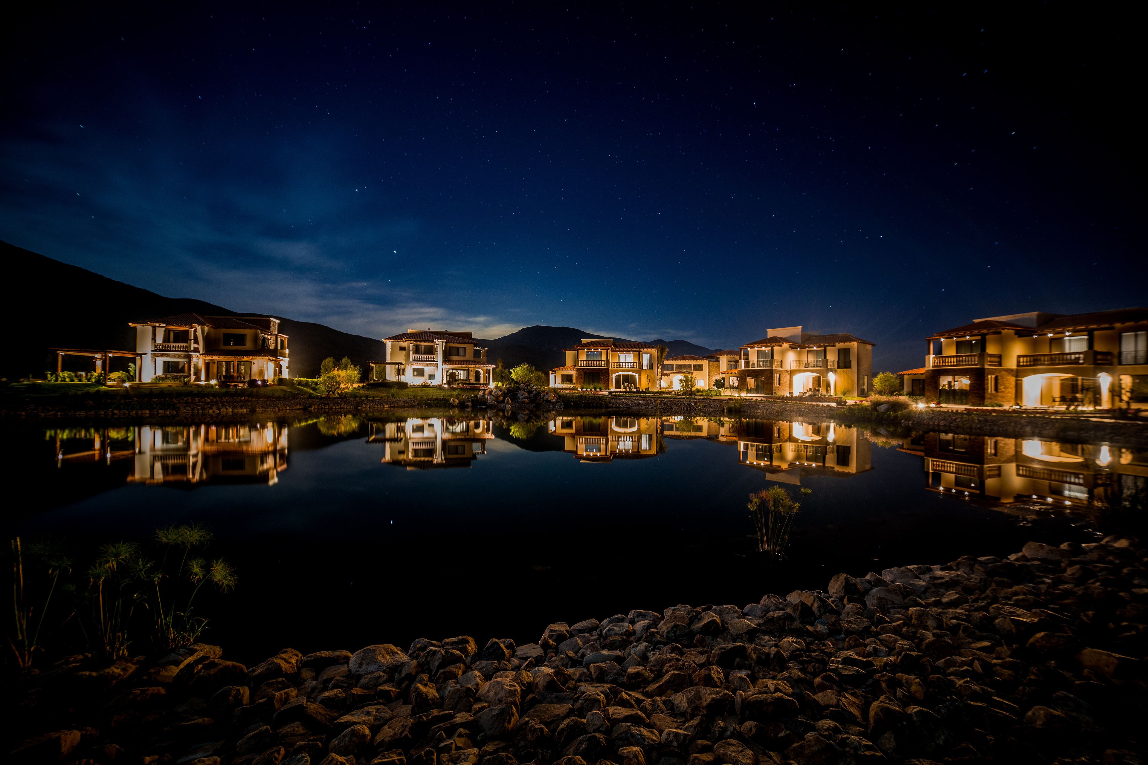 Ein Hotel am See mit mehreren Gebäuden, einem ruhigen See und einem sternenübersäten Nachthimmel.