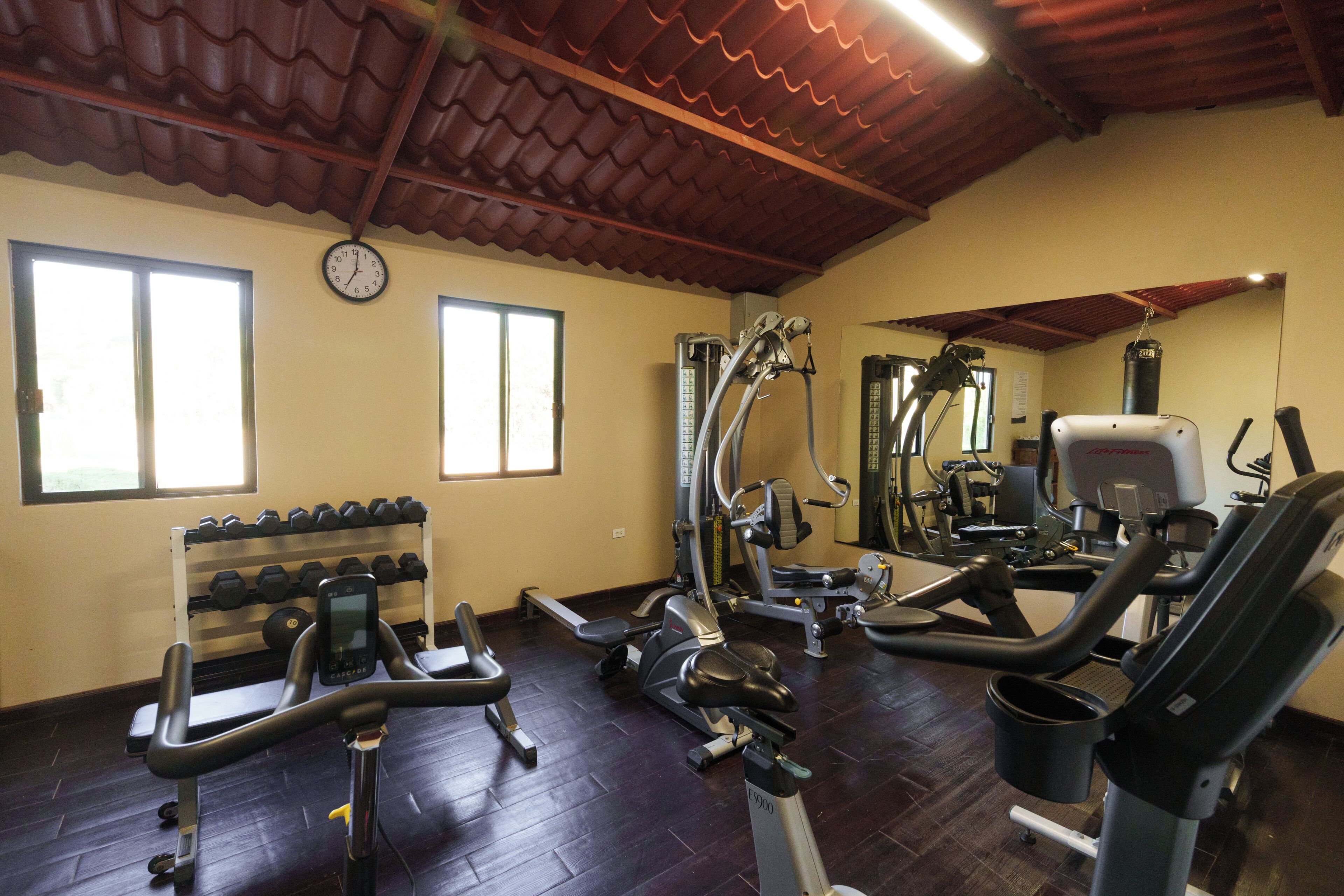 Un gimnasio con máquinas de cardio, mancuernas y un reloj en la pared.